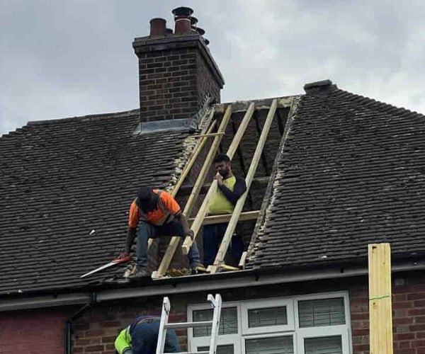 This is a photo of a roof repair being carried out. A section of the roof has been stripped and two roofers are replacing the rafters. Works being carried out by TVB Roofing