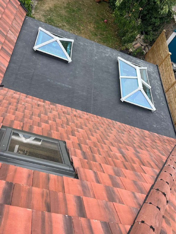 This is a photo taken from the roof ridge looking down a tiled pitched roof on to a flat roof.